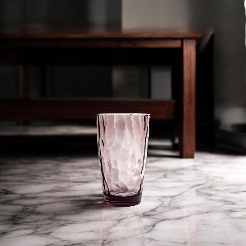 Puede incluir: Un vaso de color rosa claro con una textura geom&eacute;trica facetada en su superficie exterior. El vaso presenta una forma cil&iacute;ndrica que se estrecha ligeramente hacia la base, con un borde liso y una base de color rosa m&aacute;s oscuro.