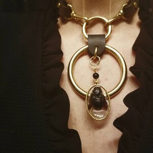May include: A gold chain choker necklace with a large gold ring and a smaller oval pendant containing a preserved insect. The pendant is attached to the ring with a small chain and a black bead.