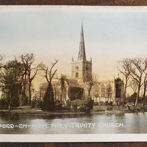 May include: A vintage postcard depicting Holy Trinity Church in Stratford-upon-Avon, England. The church is a large, stone building with a tall spire and a pond in the foreground.