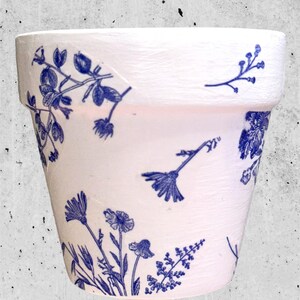 May include: A white ceramic flower pot with a blue floral pattern. The pot is a classic design with a rounded bottom and a wide opening.