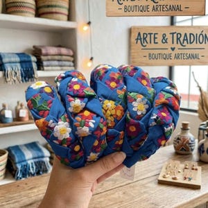 Puede incluir: Diademas de tela azul con bordados florales coloridos. Las diademas se exhiben sobre una superficie de madera, con un letrero que dice "ARTE & TRADICI&Oacute;N - BOUTIQUE ARTESANAL" al fondo. Se ven otros art&iacute;culos artesanales.
