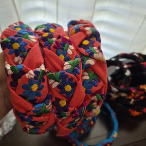 Puede incluir: Diademas trenzadas en tela coral, adornadas con patrones florales bordados en azul, amarillo y blanco. Tambi&eacute;n se ven diademas adicionales en azul y negro con dise&ntilde;os florales. Estos accesorios son perfectos para a&ntilde;adir un toque de color y estilo.