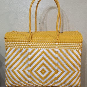 May include: A woven tote bag in a vibrant yellow and white geometric pattern. The bag features a rectangular shape with two sturdy handles. The design incorporates a diamond pattern, creating a visually appealing accessory.