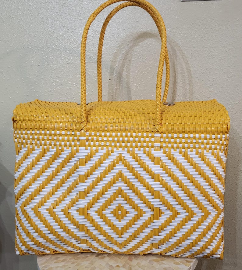 May include: A woven tote bag in a vibrant yellow and white geometric pattern. The bag features a rectangular shape with two sturdy handles. The design incorporates a diamond pattern, creating a visually appealing accessory.