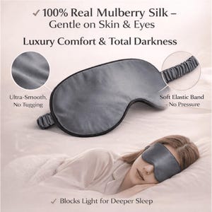 Op de afbeelding: Een grijze zijden slaapmasker met zwarte rand en elastische band. Het masker is ontworpen voor luxe comfort en totale duisternis. Tekst op de afbeelding luidt "100% Real Mulberry Silk - Gentle on Skin & Eyes" en "Blocks Light for Deeper Sleep."