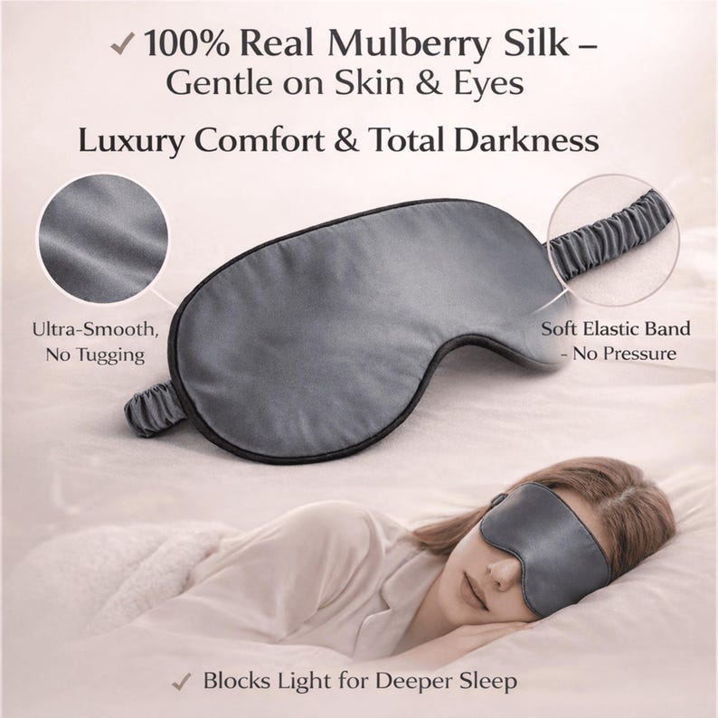 Op de afbeelding: Een grijze zijden slaapmasker met zwarte rand en elastische band. Het masker is ontworpen voor luxe comfort en totale duisternis. Tekst op de afbeelding luidt "100% Real Mulberry Silk - Gentle on Skin & Eyes" en "Blocks Light for Deeper Sleep."