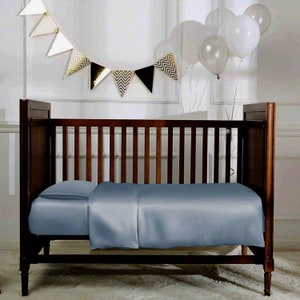 May include: A wooden crib with a blue fitted sheet. The crib is in a room with white walls and a gold and black banner hanging above it.