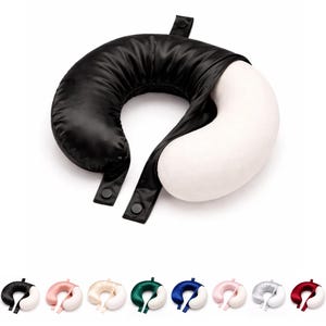 May include: A black and white travel pillow with a U-shape design. The black section is made of a shiny material, and the white section is a soft, plush fabric. The pillow has two black straps with snap closures. Several other colour variations are shown below.