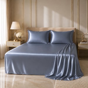 May include: A bed dressed with a set of blue-grey satin sheets and two matching pillowcases. The sheets have a lustrous sheen, and the fabric drapes elegantly over the bed. The bedding set is a luxurious addition to any bedroom.