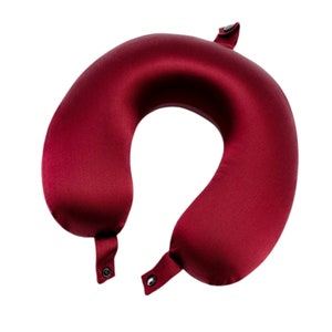 May include: A burgundy travel neck pillow with a contoured shape for head and neck support. The pillow has adjustable straps for a secure fit.
