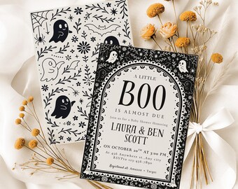 May include: Two Halloween-themed baby shower invitations. One features a black and white pattern of ghosts, bats, and floral elements. The other says "A Little Boo Is Almost Due" with event details. Dried flowers and a white ribbon accent the cards.