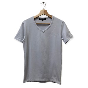 May include: A light gray v-neck t-shirt with a white graphic design on the front. The graphic design is a simple line drawing of a triangle with a small text label that says "always" inside the triangle.