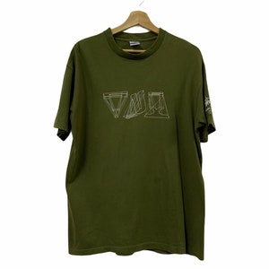 Könnte beinhalten: Ein grünes T-Shirt mit einem weißen geometrischen Muster und dem Wort "VIVA" auf der Vorderseite. Das T-Shirt hat einen Rundhalsausschnitt und kurze Ärmel.