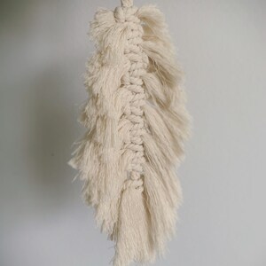 May include: A white macrame feather wall hanging with a fringe detail.