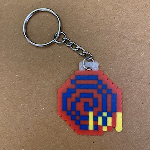 May include: A red, blue, and yellow pixelated keychain with a spiral design. The keychain is attached to a silver key ring.