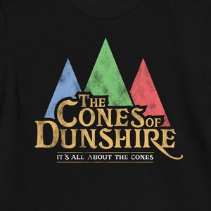 May include: Black t-shirt featuring a vintage-style graphic of three colourful cones and the text "The Cones of Dunshire" in gold lettering. The text "It's all about the cones" is printed below the graphic.