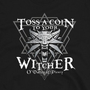 May include: Black t-shirt with a white graphic of a wolf's head in a triangle with the text "Toss a coin to your Witcher O'Valley of Plenty".