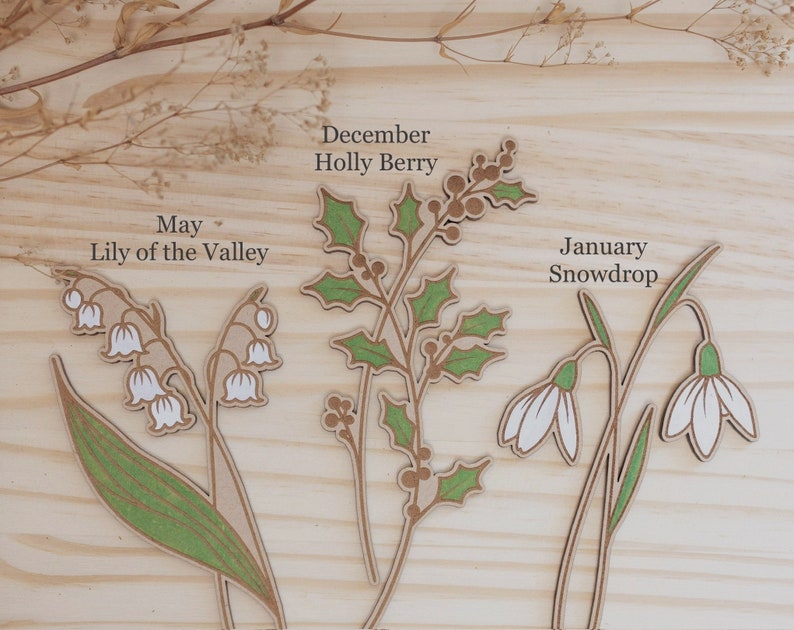 White birth month flowers are May lily of the Valley and January snowdrop. December is green leaves with engraved holly berries