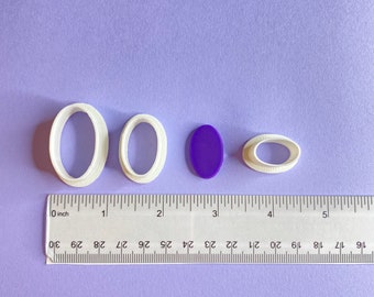 May include: Four white plastic cookie cutters in the shape of ovals, with one cutter being a smaller size than the other three. The cutters are on a purple surface with a white ruler measuring 6 inches.