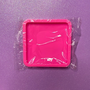 Op de afbeelding: Een roze siliconen mal in een doorzichtige plastic zak. De mal is vierkant met afgeronde hoeken en is ontworpen voor het gieten van hars.