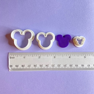 Peut inclure: Trois emporte-pièces en plastique blanc en forme de tête de Mickey Mouse. Les emporte-pièces sont de tailles différentes, le plus grand mesurant 5 cm de diamètre. Une règle est incluse pour l'échelle.