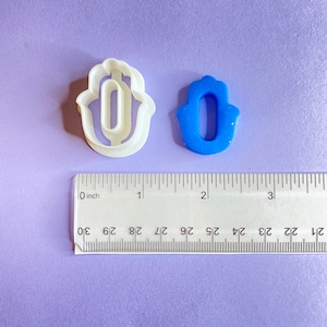 May include: Two hamsa hand cookie cutters, one white plastic and one blue plastic. The cutters are approximately 1 inch in size.