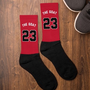 May include: A pair of red and black socks with the text "The Goat 23" printed on them.