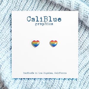 May include: A pair of rainbow heart-shaped stud earrings on a white card with the text "CaliBlue graphics" and "handmade in Los Angeles, California".