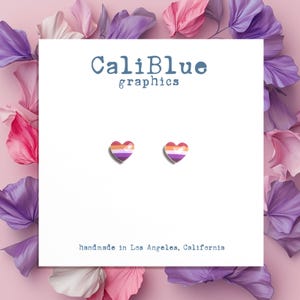 May include: A pair of small heart-shaped earrings with a lesbian pride flag design. The earrings are on a white card with the text "CaliBlue graphics" and "handmade in Los Angeles, California".