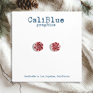 May include: A pair of red and white candy cane swirl stud earrings. The earrings are handmade in Los Angeles, California.