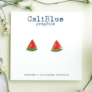 May include: A pair of watermelon slice stud earrings. The earrings are red, green, and black with a white background. The earrings are handmade in Los Angeles, California. CaliBlue graphics.