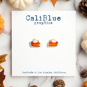 May include: A pair of pumpkin pie slice earrings with white frosting on a white card with the text "CaliBlue graphics" and "handmade in Los Angeles, California".