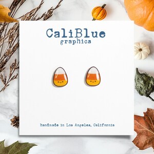 May include: A pair of candy corn earrings with a white, orange, and yellow design. The earrings are handmade in Los Angeles, California. CaliBlue graphics.