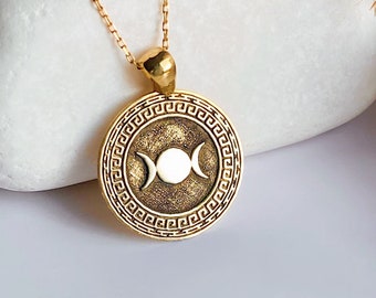 May include: A gold necklace with a round pendant featuring a triple moon symbol surrounded by a Greek key design.