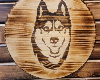 May include: A round wooden plaque with a detailed pyrography image of a smiling husky dog. The wood has a natural grain and a glossy finish. The dog's features are carefully burned into the wood, creating a rustic, handcrafted look.