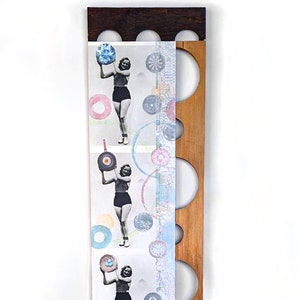 May include: A wooden panel with a series of circular cutouts. The panel is decorated with a collage of images, including a woman holding a variety of round objects, and a variety of colorful circles and patterns.