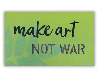 Może przedstawiać: Zielony drewniany znak z napisem "make art not war" czarnymi literami. Znak ma jasnozielony wzór liści w tle.
