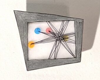 May include: A grey framed picture with a white background and black lines radiating from the centre. There are three coloured circles in the picture: a blue circle, a pink circle, and an orange circle.