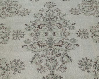 Könnte beinhalten: Hellgrüner und brauner gemusterter Teppich mit einem zentralen Medaillon-Design und floralen Motiven. Der Teppich hat ein verwaschenes, Vintage-Aussehen mit verblassten Farben und aufwendigen Details. Das Gesamtdesign ist symmetrisch und traditionell.