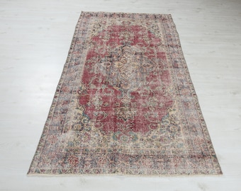May include: A vintage red rug with a faded floral pattern and a distressed look. The rug has a cream border with a blue and green floral design.