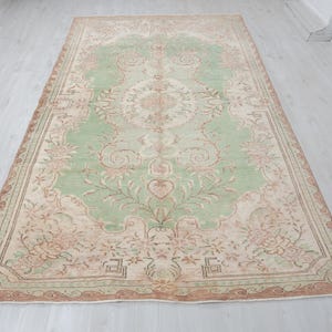 May include: A large, rectangular area rug with an intricate floral pattern. The rug features a central field of light green, surrounded by a border of beige and brown. Floral and vine motifs are spread across the surface.