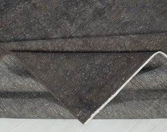 May include: Close-up of a dark grey rug with a white fringe. The rug is folded in half, showing the underside of the fabric.