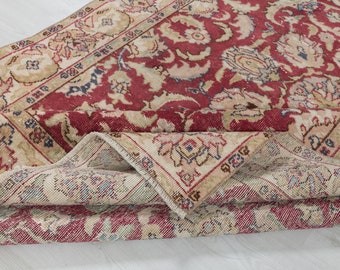 May include: A vintage rug with a red background and a floral pattern. The rug is folded in half, showing the beige underside.