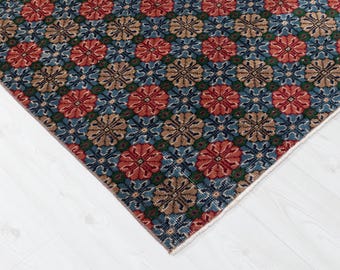 May include: A patterned rug fragment with a repeating floral design. The rug has a blue background with red, brown, and green floral patterns. The rug's edge is visible, showing a white border.