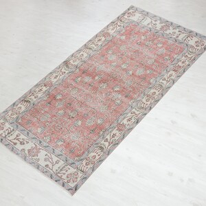 May include: A vintage rug with a pink floral pattern and a cream border. The rug has a distressed look and is perfect for adding a touch of bohemian style to your home.