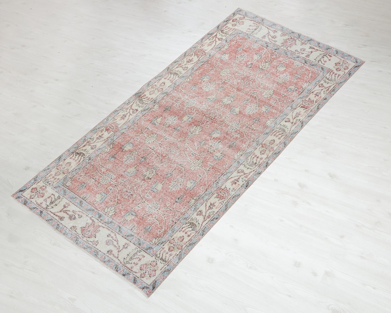 May include: A vintage rug with a pink floral pattern and a cream border. The rug has a distressed look and is perfect for adding a touch of bohemian style to your home.