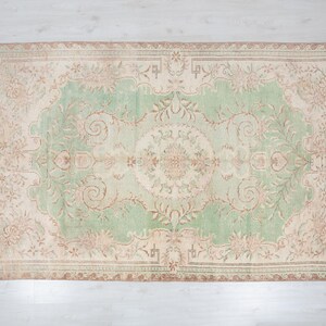 May include: Rectangular area rug with a central green field and a beige border. The rug features an intricate floral pattern in shades of beige, brown, and green. The rug's design is symmetrical, with a central medallion and corner accents.