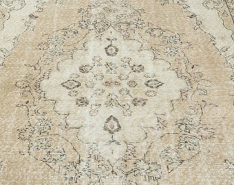 May include: A beige vintage rug with a faded floral pattern in brown. The rug has a distressed look and a worn texture.