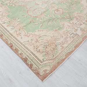 May include: A vintage area rug with a distressed, floral design. The rug features a central field of pale green with floral motifs in shades of pink and beige. The border is a darker brown with a repeating pattern.