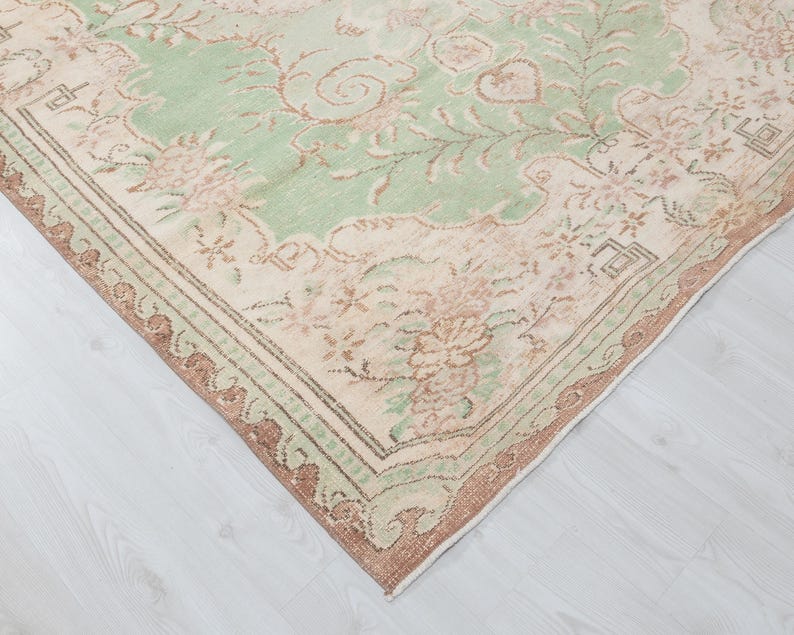May include: A vintage area rug with a distressed, floral design. The rug features a central field of pale green with floral motifs in shades of pink and beige. The border is a darker brown with a repeating pattern.